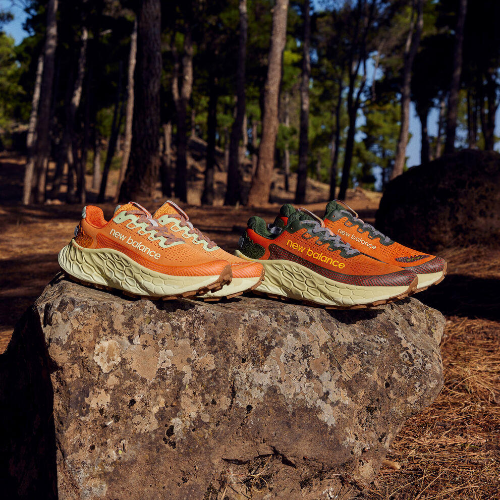 Two pairs of orange trail shoes sitting on a rock in the woods.  