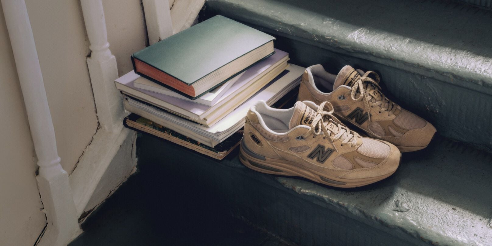 Un par de tenis Made in UK de New Balance en una escalera, junto a una pila de libros.&nbsp;