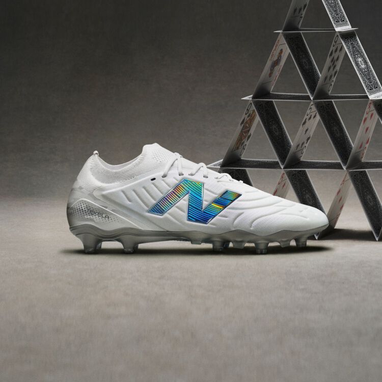 Side profile shot of white cleats with blue accents placed in front of a pyramid of cards.