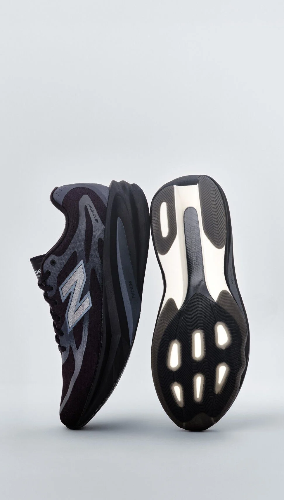 A pair of black New Balance sneakers sitting on a gray studio backdrop. 