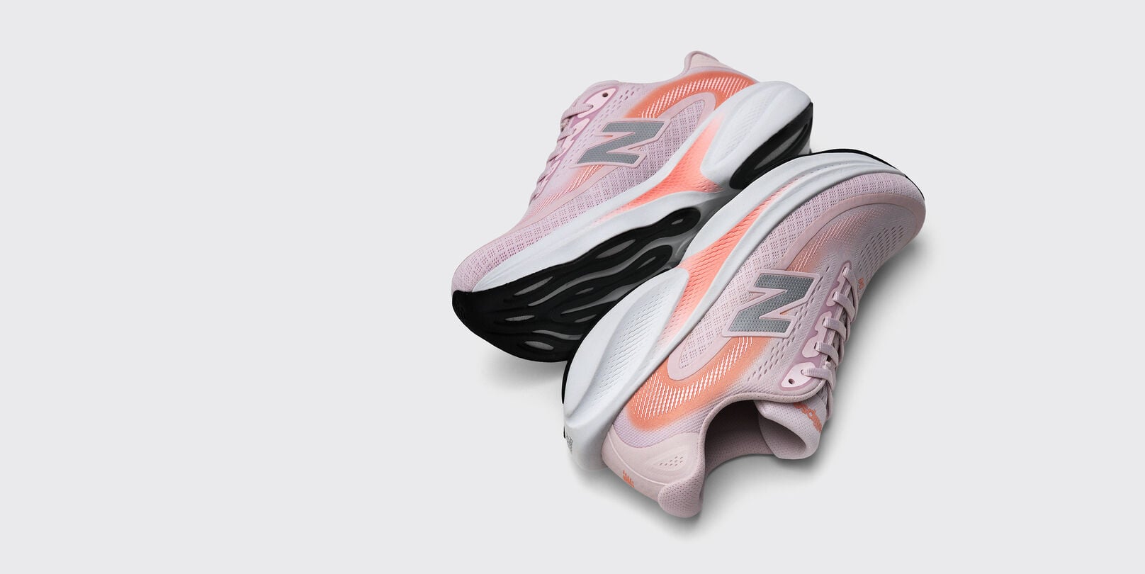 Pair of light pink New Balance running shoes with coral accents and chunky black-and-white soles displayed on a light gray background. 
