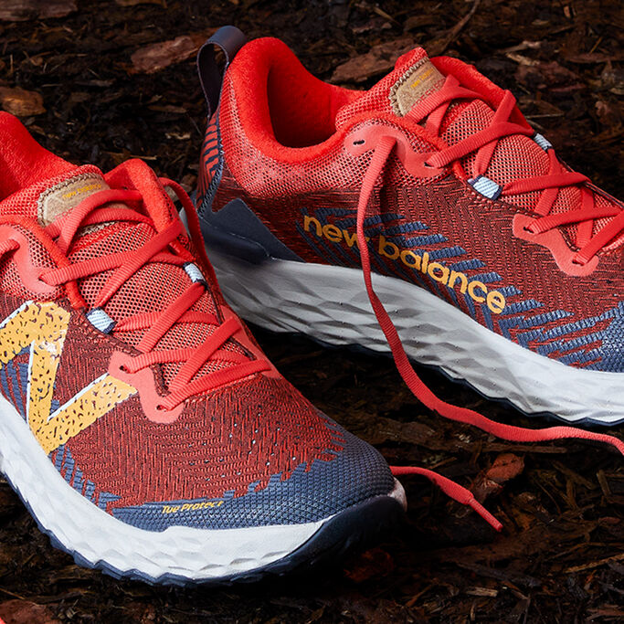 Close detail image of the pair of shoes with the laces untied sitting on dirt. 