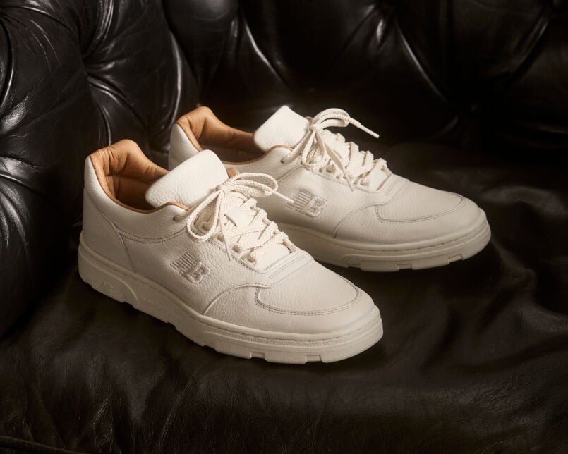 Knee down view of a woman wearing a pair of New Balance Made in UK sneakers standing in a beige studio environment.
