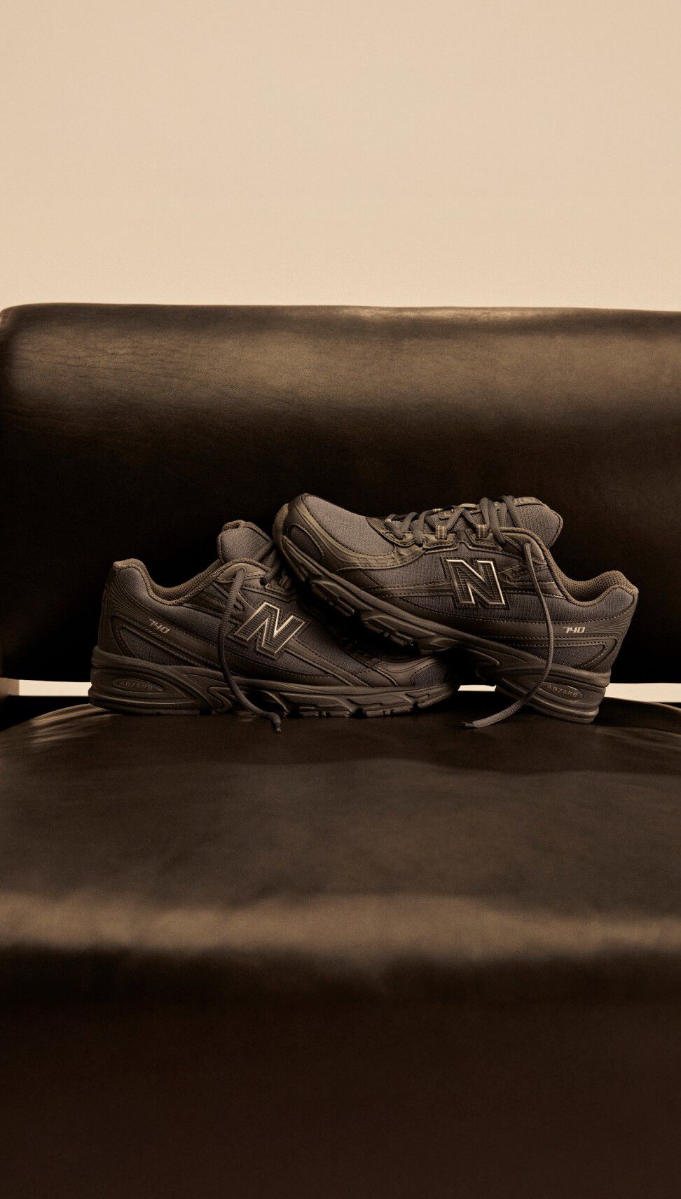 Dark New Balance 740 shoes on top of a dark leather and wooden chair.