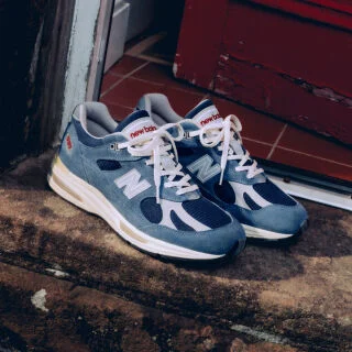 A pair of New Balance Made in UK sneakers sitting on an old stone doorstep next to a red door. 