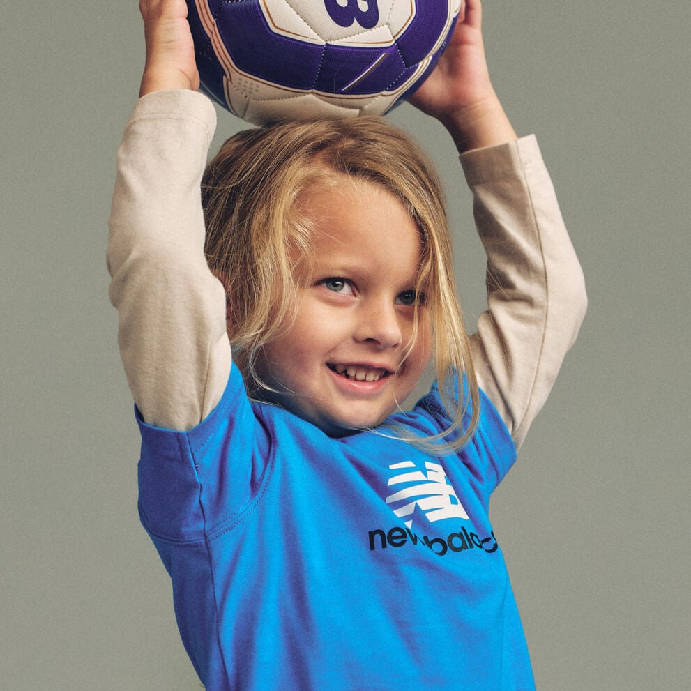 Imagen de estudio en primer plano de un ni&ntilde;o sosteniendo un bal&oacute;n de f&uacute;tbol azul, blanco y morado por encima de la cabeza con ambas manos.