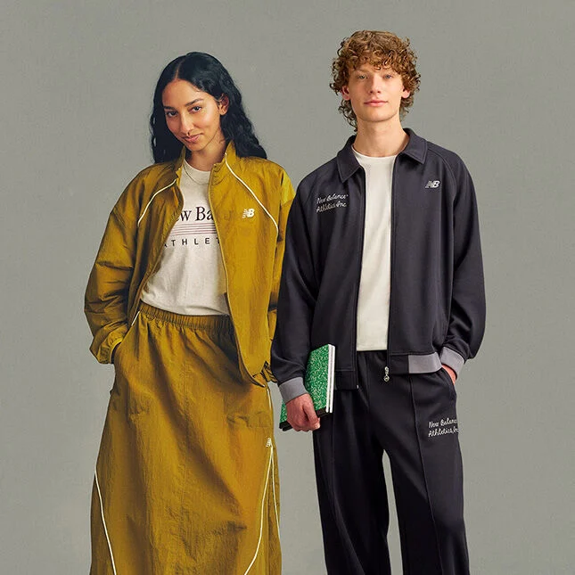 Two people stand side by side against a plain light gray studio background in a clean, minimal composition with ample empty space below.