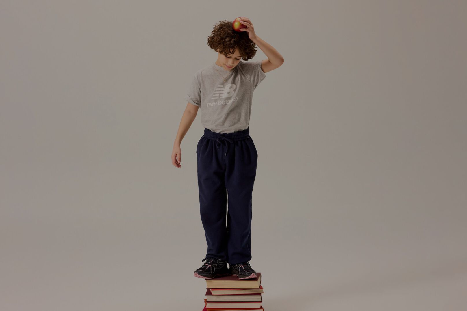 Niño parado sobre libros sosteniendo una manzana sobre su cabeza.