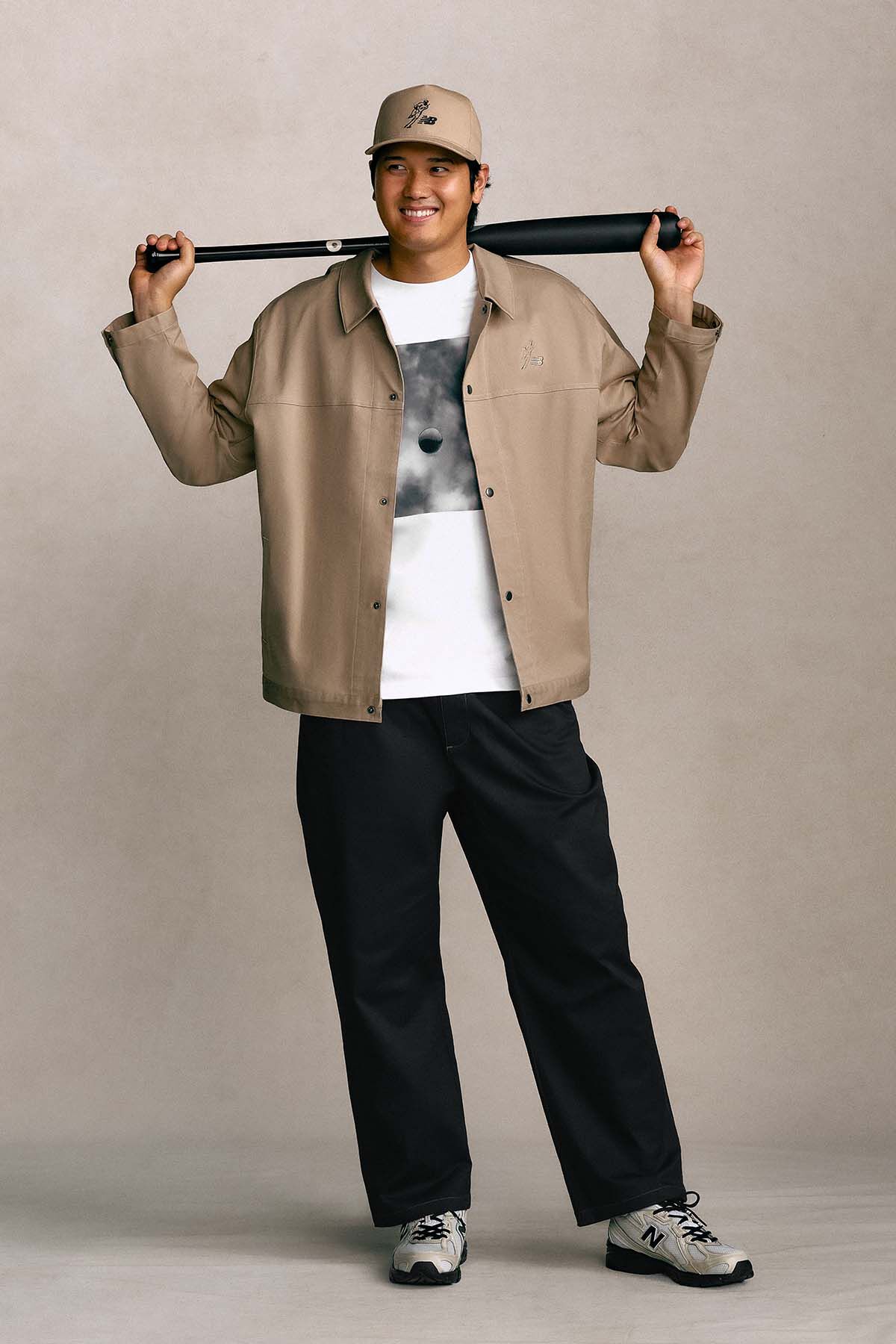 Shohei Ohtani standing against a tan studio backdrop holding a baseball bat.